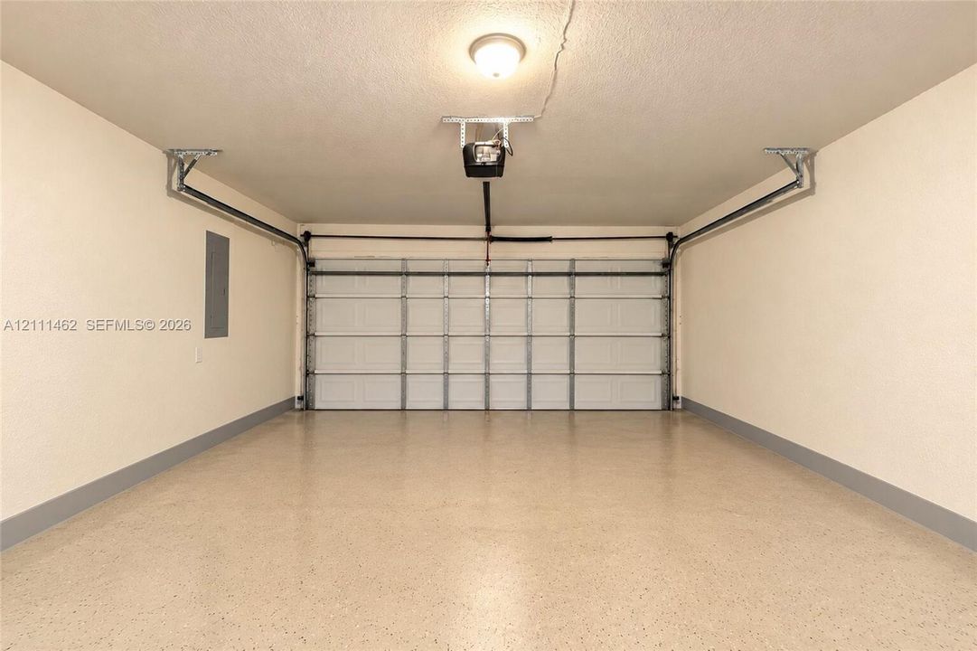 Finished garage featuring a white sectional garage door, epoxy-coated flooring, neutral wall paint, and a ceiling-mounted automatic door opener