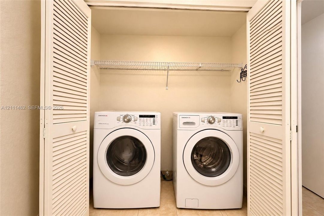 Laundry closet featuring white louvered bifold doors, wire shelving, and tile flooring