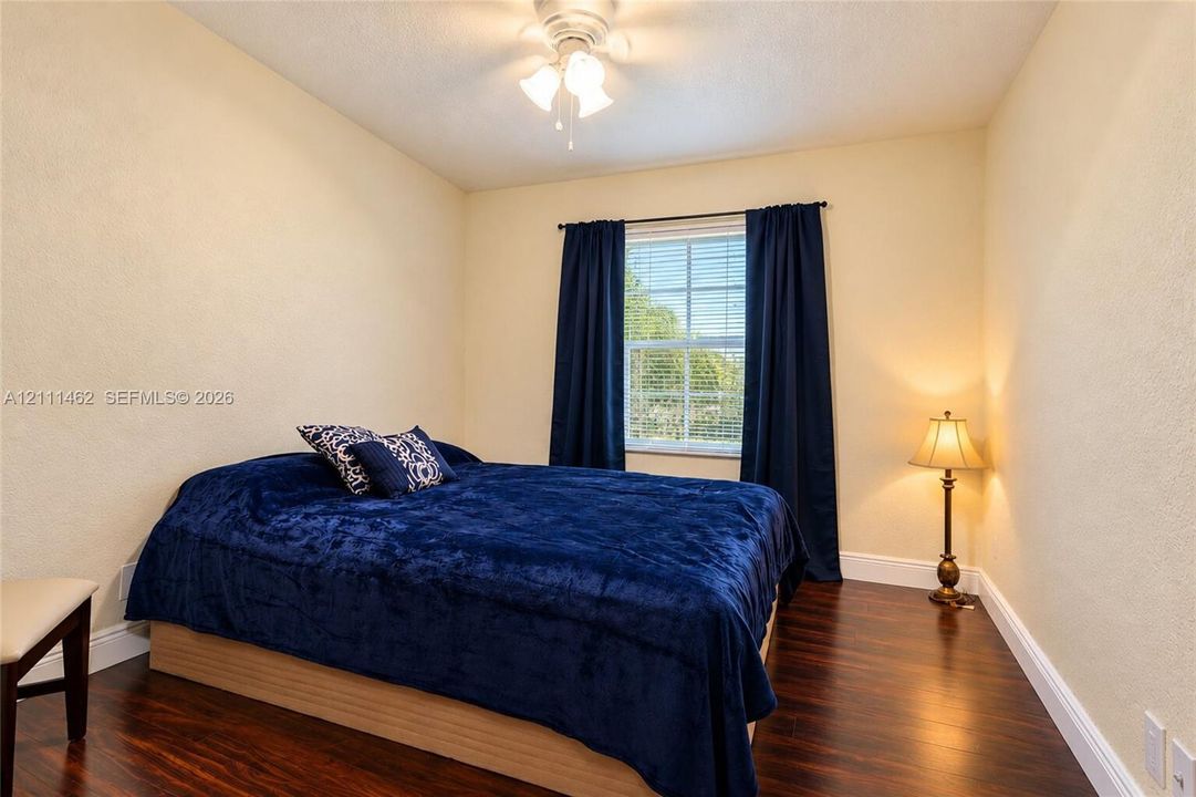 Wood-finish flooring, single-hung window with horizontal blinds, and a central ceiling-mounted light fixture with a fan