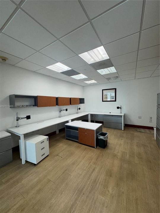 Built-in desk configuration featuring wood-finish cabinetry, integrated white countertops, drop ceiling with recessed lighting, and wood-finish flooring