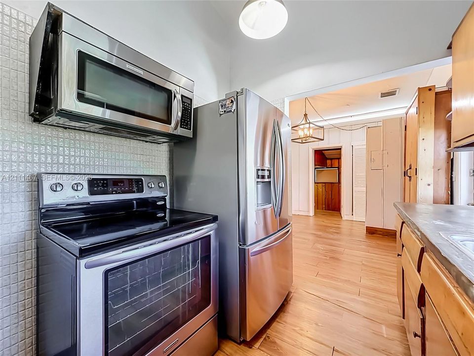 Kitchen featuring stainless steel appliances, wood-finish flooring, square-tile backsplash, and built-in cabinetry