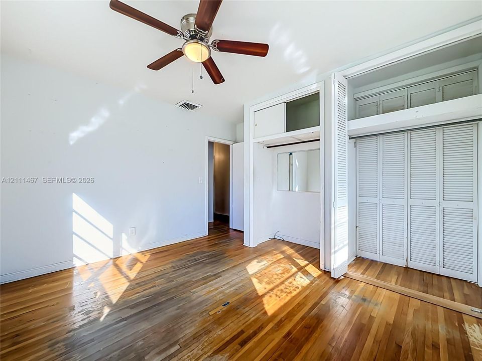 Hardwood flooring, ceiling fan with integrated lighting, and built-in closet cabinetry with louvered doors and overhead storage