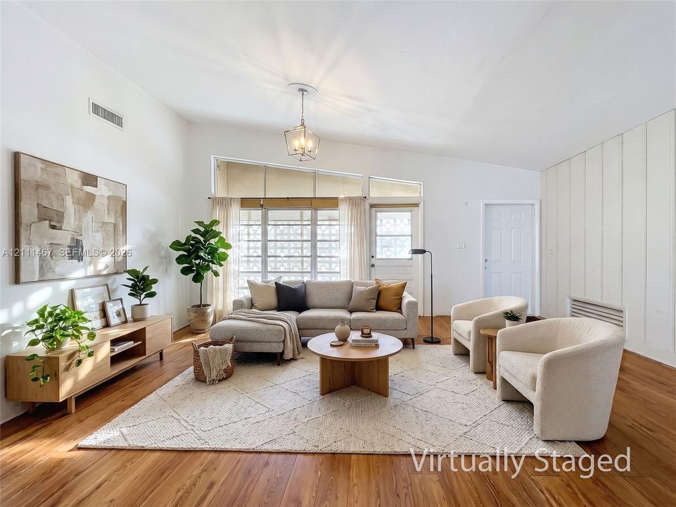 Living area featuring vaulted ceilings, wood-finish flooring, floor-to-ceiling vertical paneling, and large windows with integrated geometric decorative screens