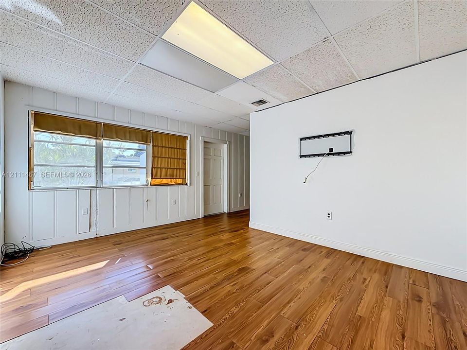Room featuring wood-finish flooring, panelled walls, a drop ceiling with integrated lighting, and a six-panel interior door