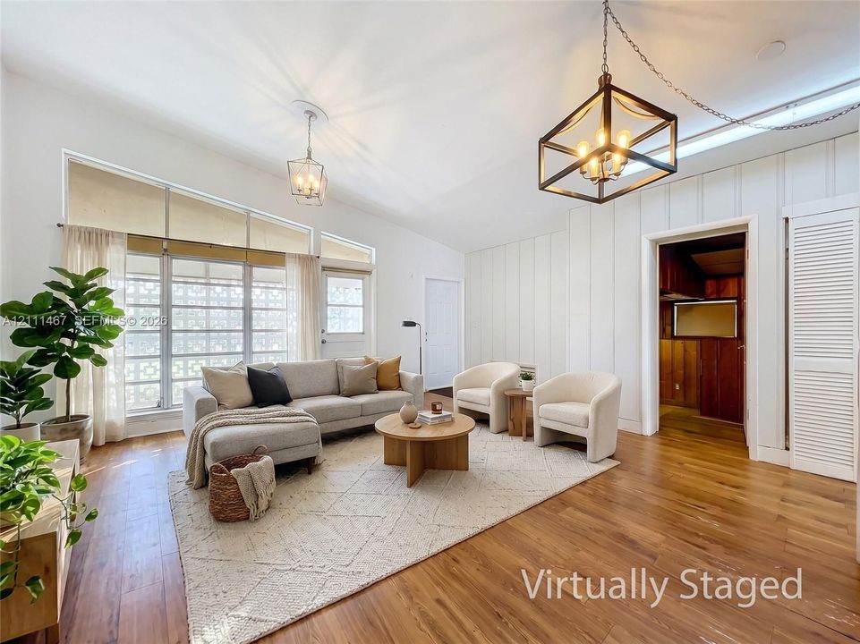 Vaulted ceilings featuring vertical shiplap wall paneling, wood-finish flooring, geometric metal frame chandelier, and expansive windows with transom accents