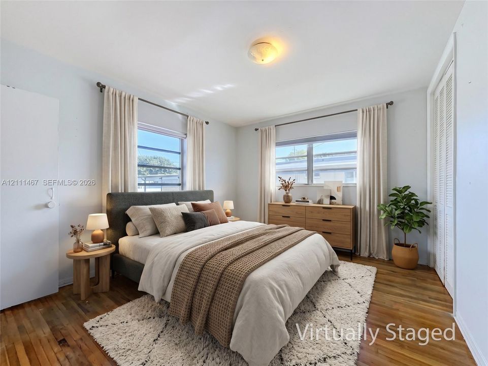 Bedroom featuring wood-finish flooring, dual windows, and louvered-door closets