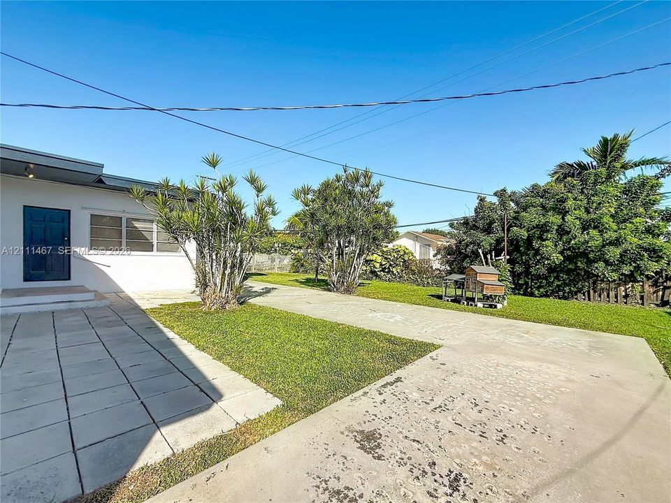 Exterior grounds featuring a concrete paved area, tiled patio, lawn space, mature landscaping, and white-painted siding