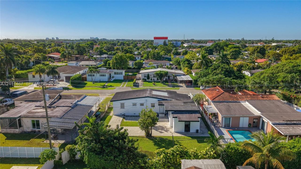 Aerial perspective of a detached single-family residence featuring a flat roofline, paved driveway, exterior lighting fixtures, and a landscaped lawn