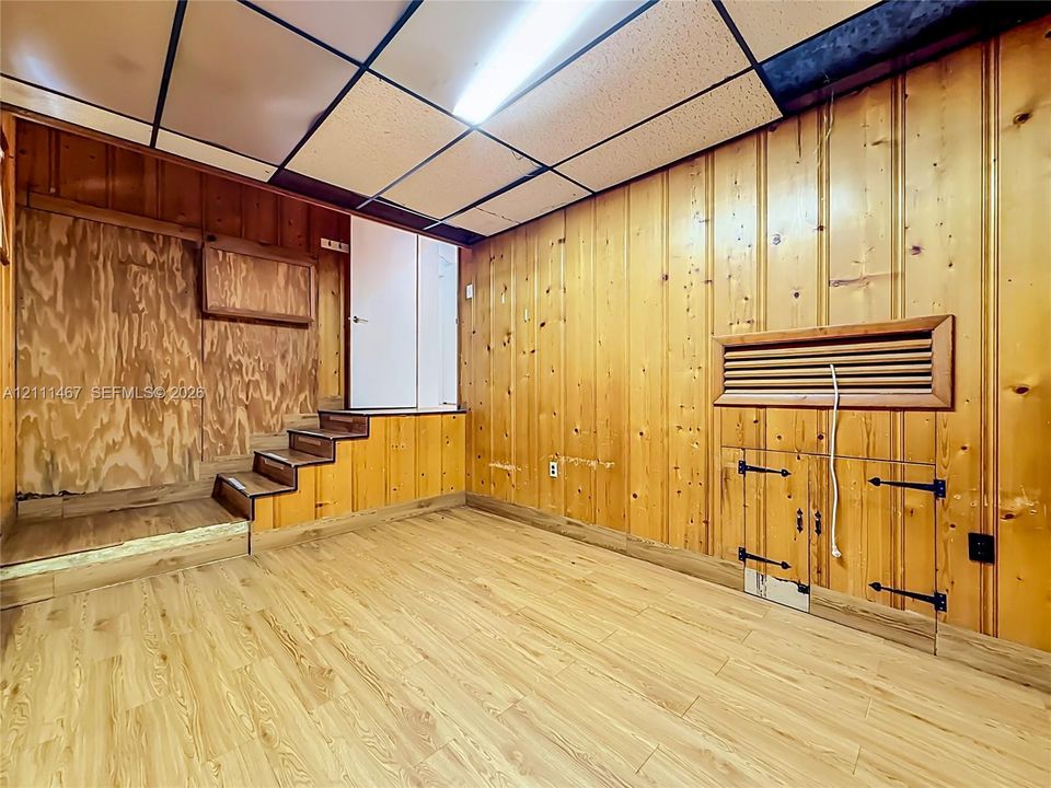 Interior space featuring natural wood wall paneling, wood-finish flooring, built-in storage cabinetry with iron hardware, and a drop ceiling with integrated lighting