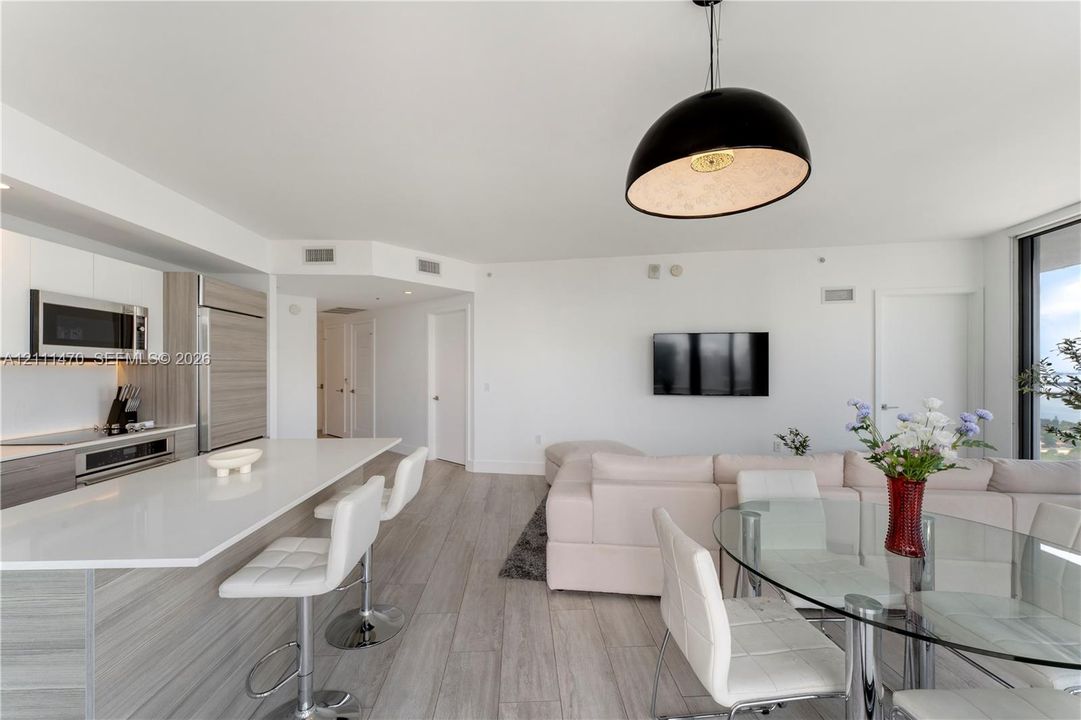 Open-concept kitchen featuring an expansive island with a quartz countertop, integrated cabinetry, stainless steel appliances, and wood-finish flooring with a dome pendant light fixture