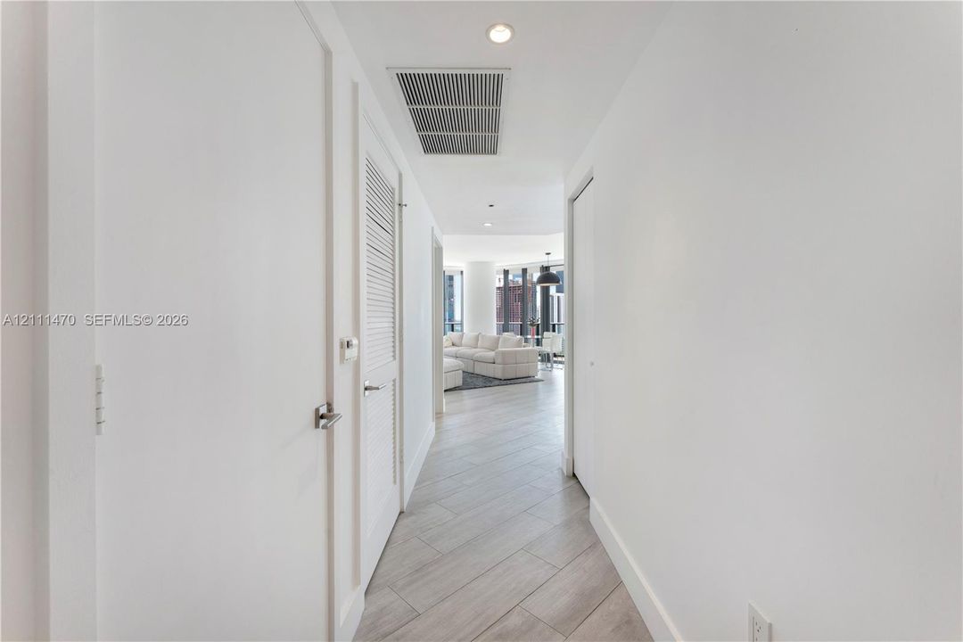 Hallway featuring neutral-tone wood-finish flooring, recessed lighting, and louvered closet doors with brushed-metal hardware
