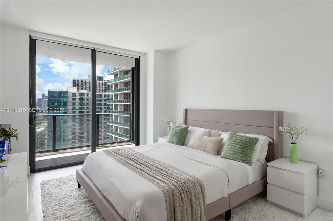 Floor-to-ceiling glass sliding doors, private balcony with metal railing, and neutral wall finishes