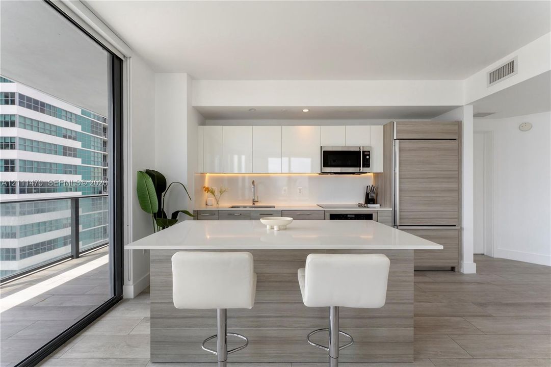 Kitchen featuring a white quartz island, high-gloss flat-panel cabinetry, integrated refrigerator, wood-finish lower cabinetry, and floor-to-ceiling glass sliding doors