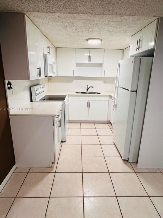 Kitchen featuring high-gloss white cabinetry, solid-surface countertops, dual-basin stainless steel sink with arch-neck faucet, and ceramic tile flooring
