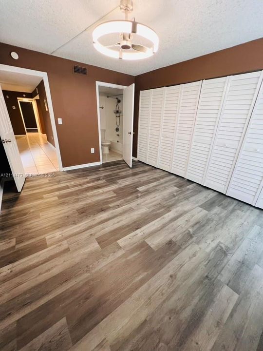 Wood-finish flooring, full-wall louvered-door closet, brushed nickel circular chandelier, and direct access to an attached bathroom