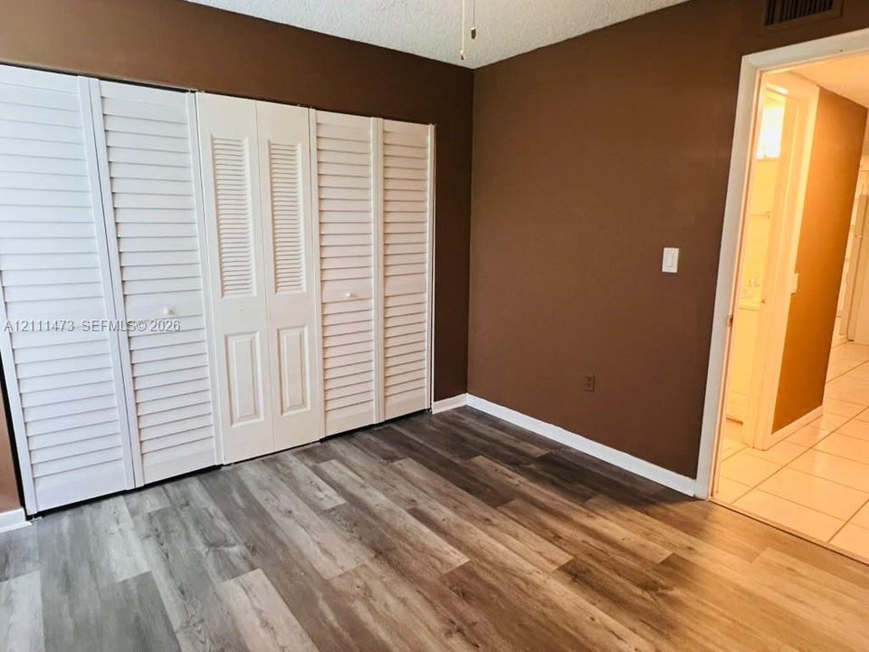 Room featuring wood-finish flooring and floor-to-ceiling white louvered-style closet doors