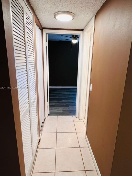 Hallway featuring ceramic tile flooring, floor-to-ceiling white louvered closet doors, and flush-mount ceiling lighting