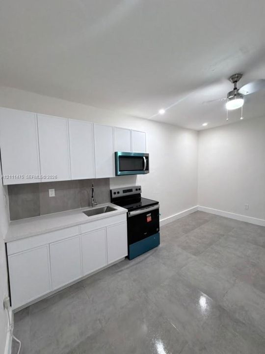Kitchen featuring matte white cabinetry, stone-finish countertops, stainless steel undermount sink, built-in microwave, and large-format tile flooring