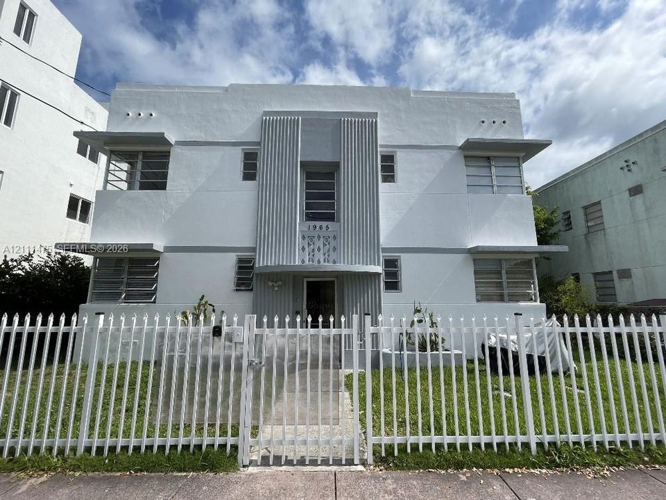 Art Deco style exterior featuring a symmetrical white facade, vertical fluted detailing, stepped architectural elements, and metal louvered windows