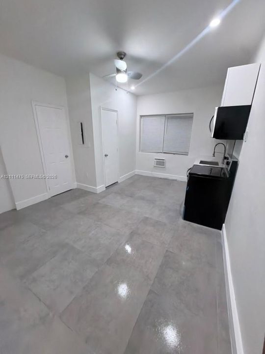 Large-format tile flooring, ceiling fan with integrated lighting, built-in kitchen cabinetry, and high-contrast kitchen appliances