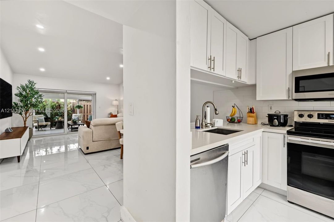Kitchen featuring white cabinetry, solid-surface countertops, subway tile backsplash, and stainless steel appliances, complemented by polished tile flooring throughout