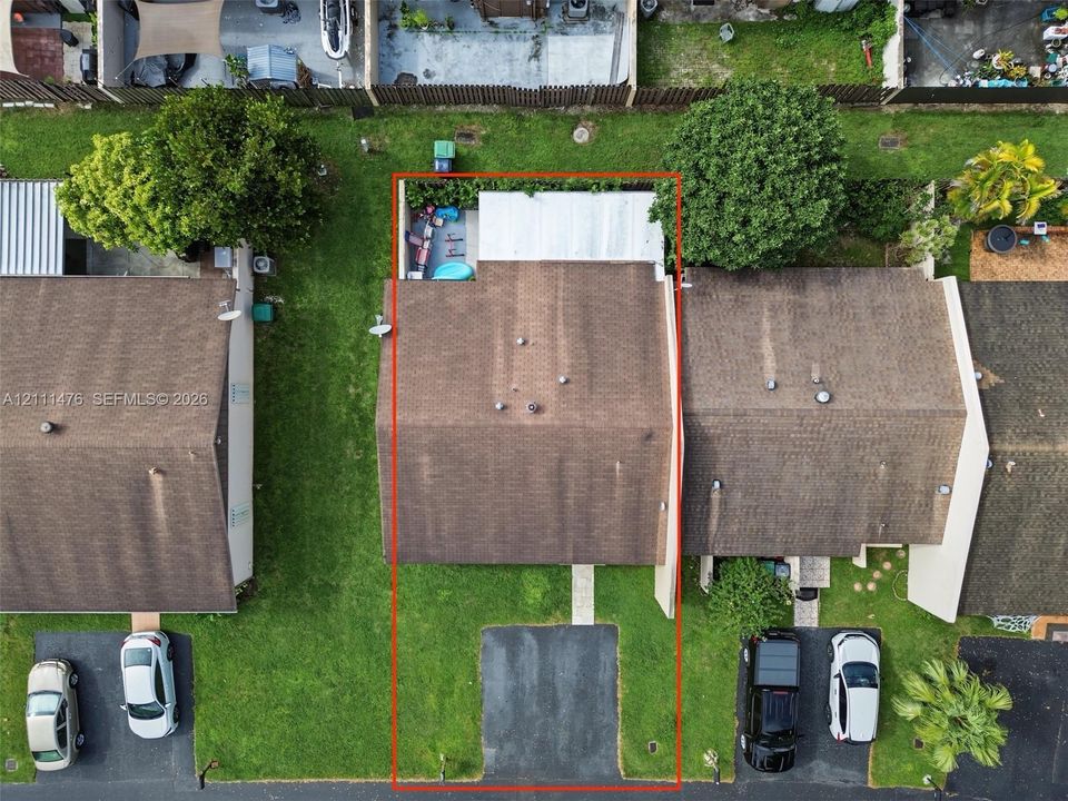 Aerial perspective featuring a shingle roof, paved driveway, concrete walkway, and private fenced rear area with a covered patio