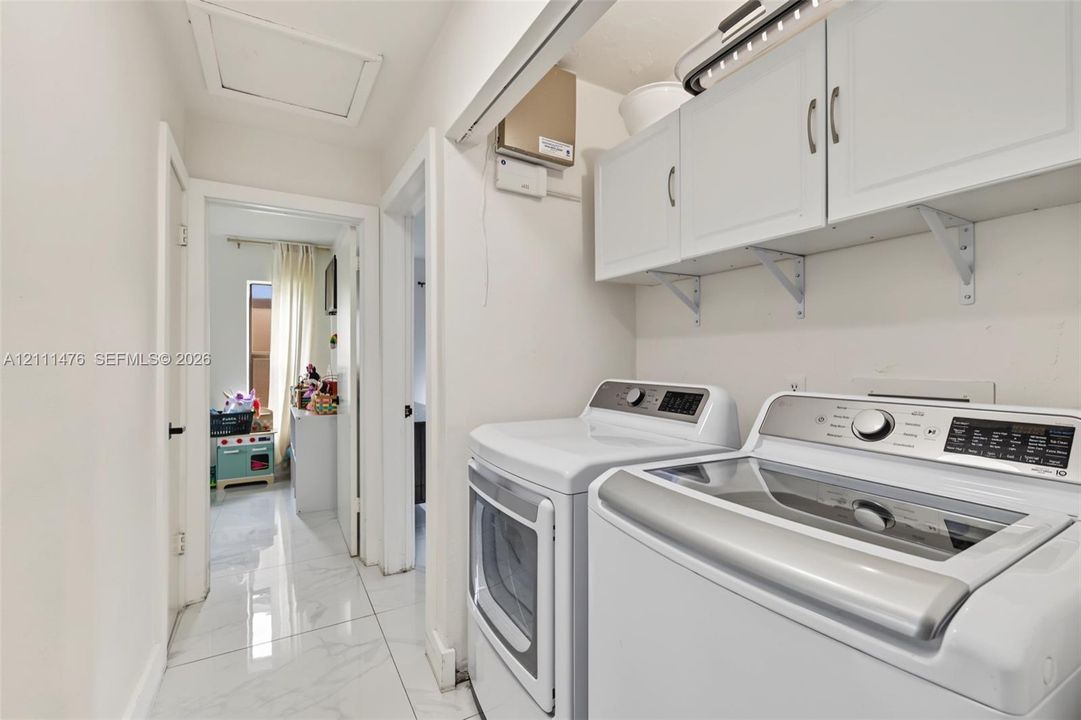 Laundry area featuring white shaker-style wall-mounted cabinetry, polished stone-finish flooring, and recessed ceiling lighting
