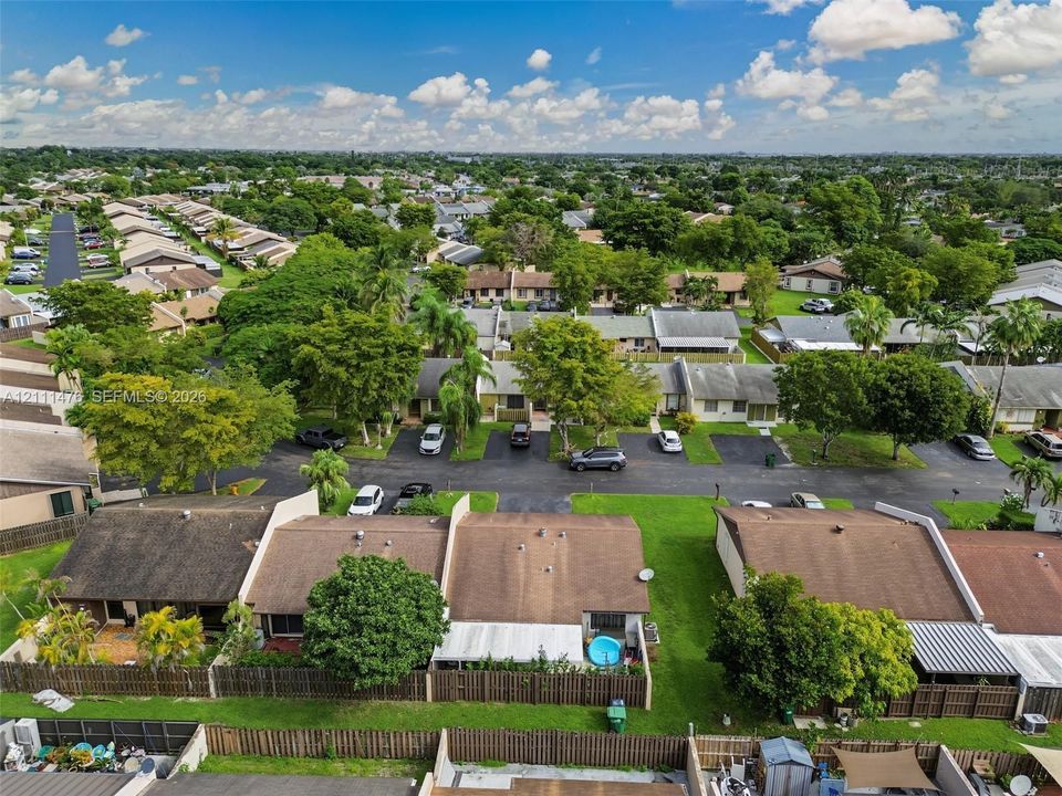 Aerial perspective of residential community featuring paved streets, mature tree canopy, shingled roofing, and fenced backyard spaces