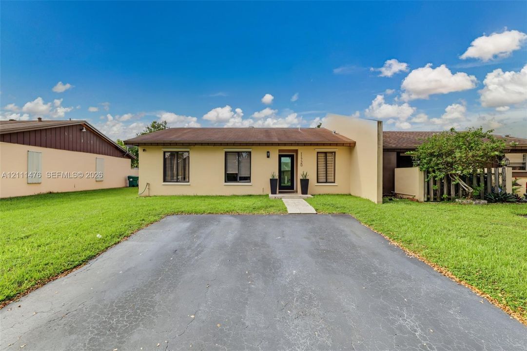 Single-story exterior featuring a paved driveway, stucco facade, and metal-frame window accents