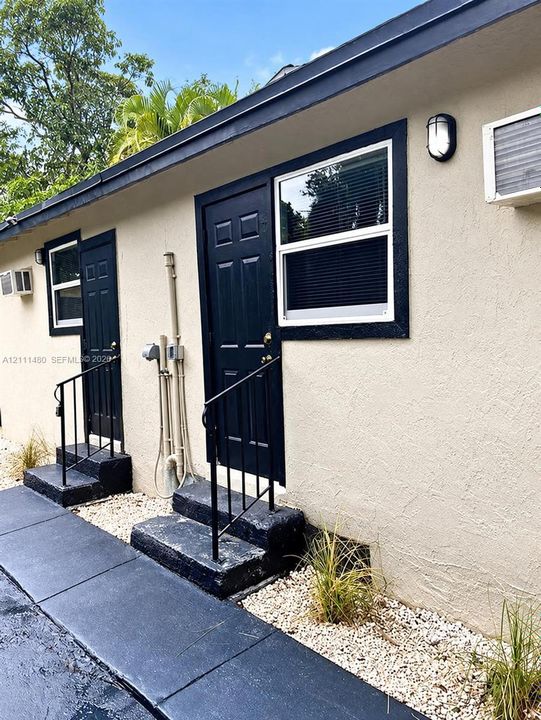 Exterior facade featuring stucco siding, black-painted doors with dark trim, metal handrails, and stone ground cover