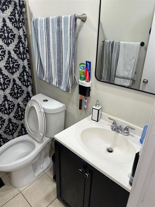 Vanity featuring a dark-toned cabinet base with a white integrated countertop and basin, dual-handle faucet, rectangular mirror with a black frame, and tiled flooring