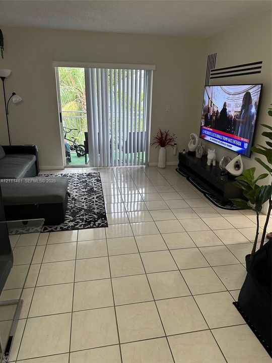 Large-format neutral tile flooring and a sliding glass door providing access to a private balcony