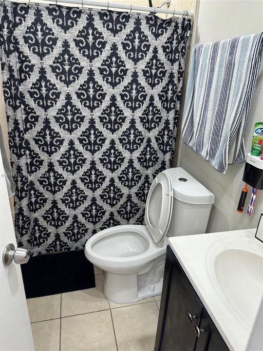 Bathroom featuring a white ceramic toilet, a vanity with a dark wood-finish cabinet and an integrated sink, and tile flooring