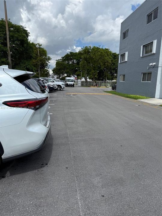 Asphalt paved surface with designated parking stalls and multi-story gray stucco exterior building