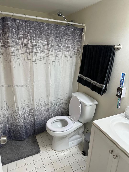 Bathroom featuring a white vanity cabinet, a drop-in sink, a standard porcelain toilet, and tile flooring