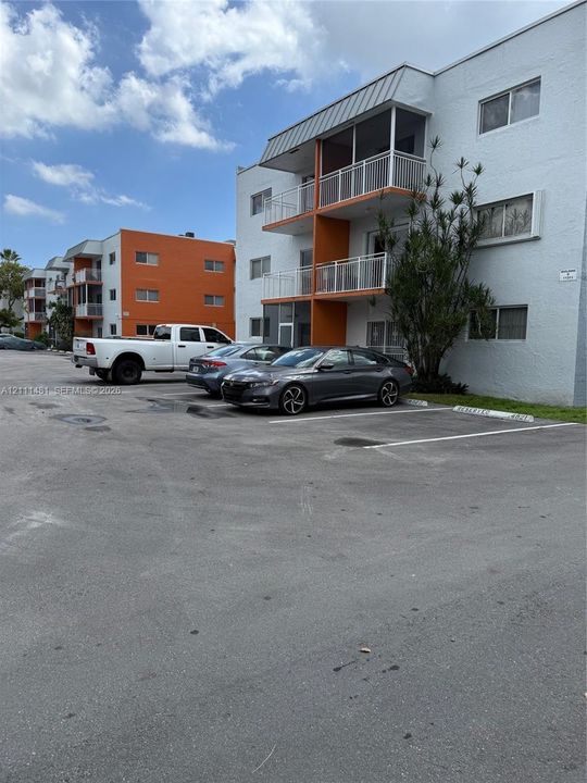 Multi-story residential building exterior featuring stucco cladding, screened balconies with metal railings, and asphalt paved surface parking