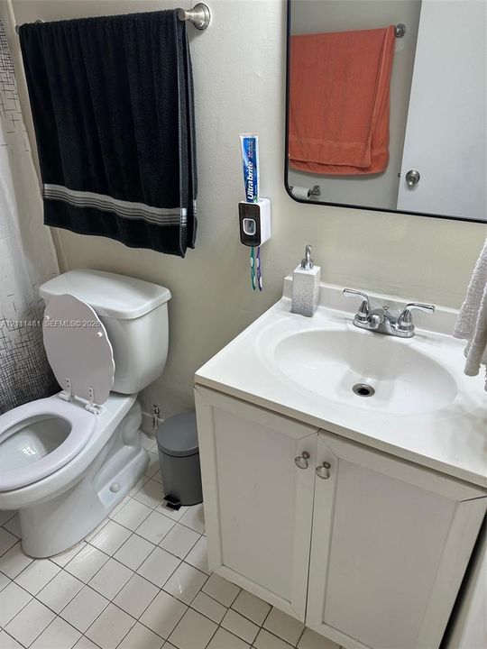 White vanity cabinet with an integrated sink, chrome double-handle faucet, rectangular wall-mounted mirror, and tile flooring