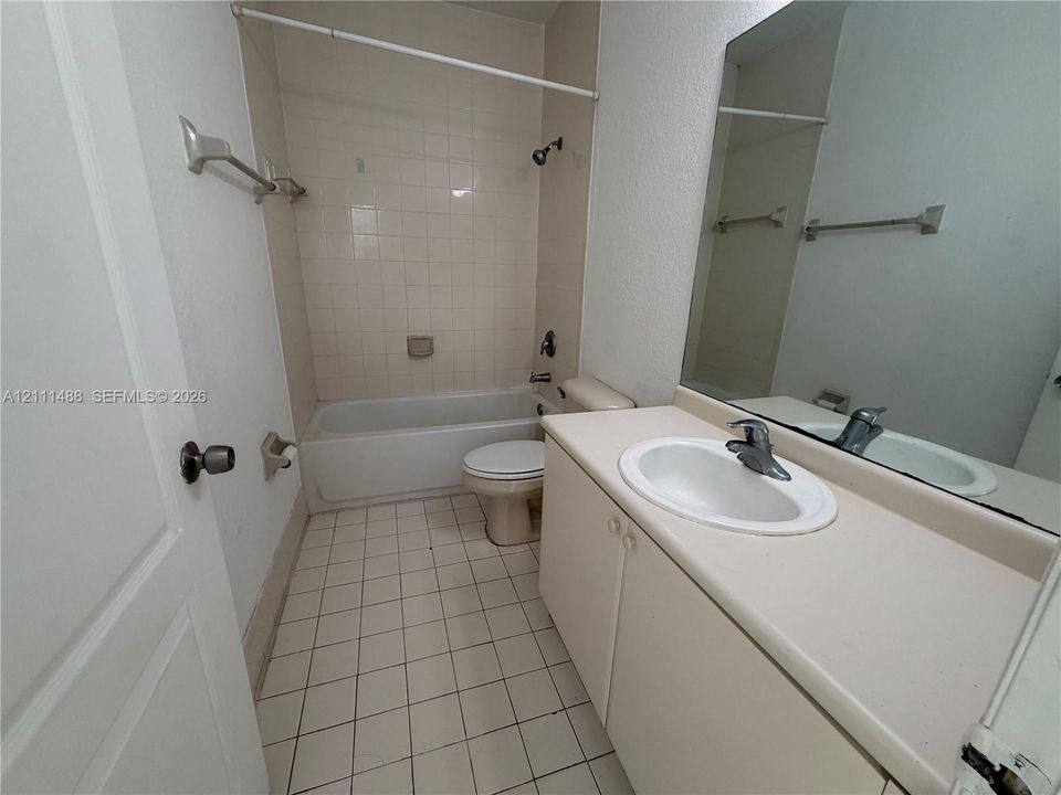 Bathroom featuring a white vanity cabinet with a solid surface countertop, integrated sink, large wall-mounted mirror, and tile flooring with matching wall tile surrounding the tub