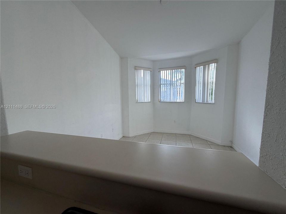 Solid surface countertop with a breakfast bar extension, three windows arranged in a bay configuration, and tile flooring