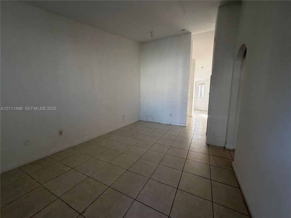 Neutral-toned ceramic tile flooring throughout, clean white wall finishes, and a distinctive arched architectural opening