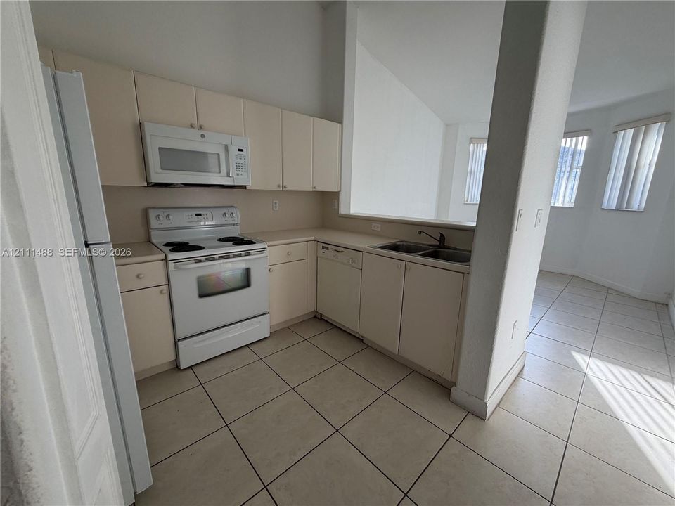 Kitchen featuring flat-panel cabinetry, a white electric range, an integrated microwave, a built-in dishwasher, and ceramic tile flooring