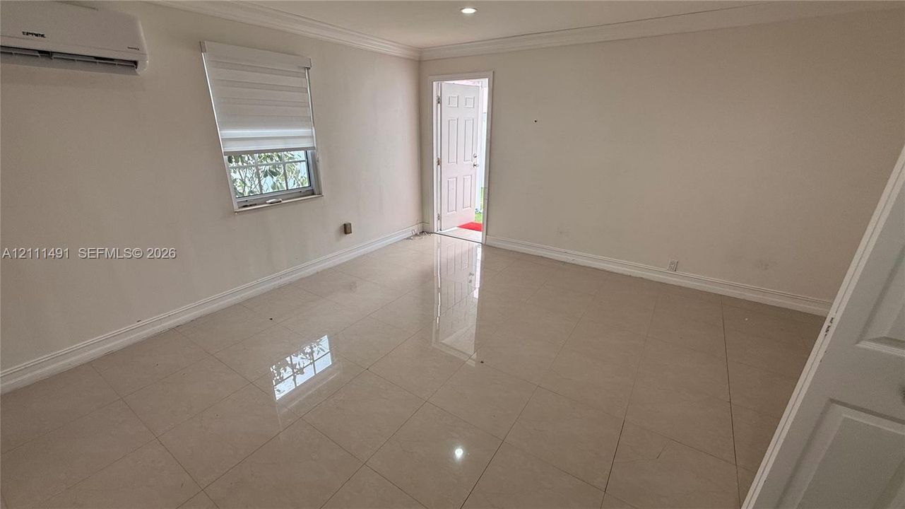 Neutral-toned interior featuring large-format tile flooring, crown molding, a wall-mounted ductless mini-split system, and recessed lighting