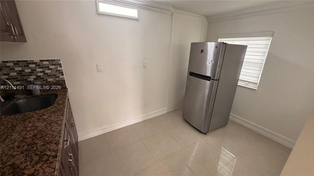 Stone-surfaced countertop, stainless steel sink, multi-tonal mosaic tile backsplash, built-in cabinetry, and tile flooring