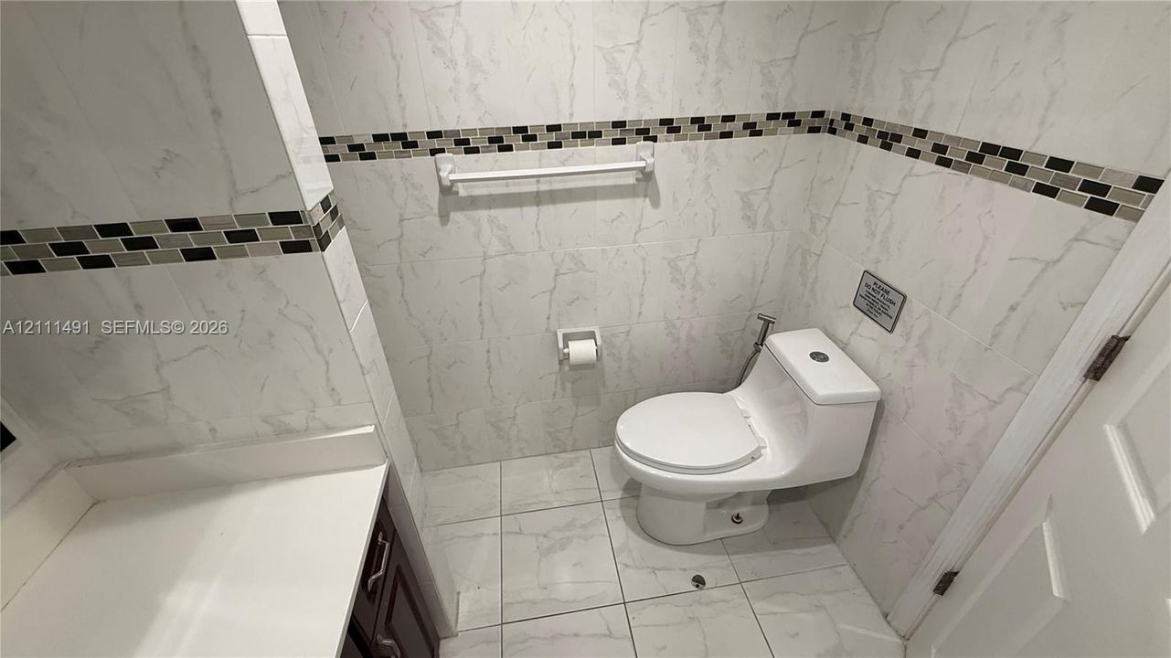 Bathroom featuring full-height wall tiling, integrated mosaic accent banding, large-format porcelain floor tile, and a one-piece toilet