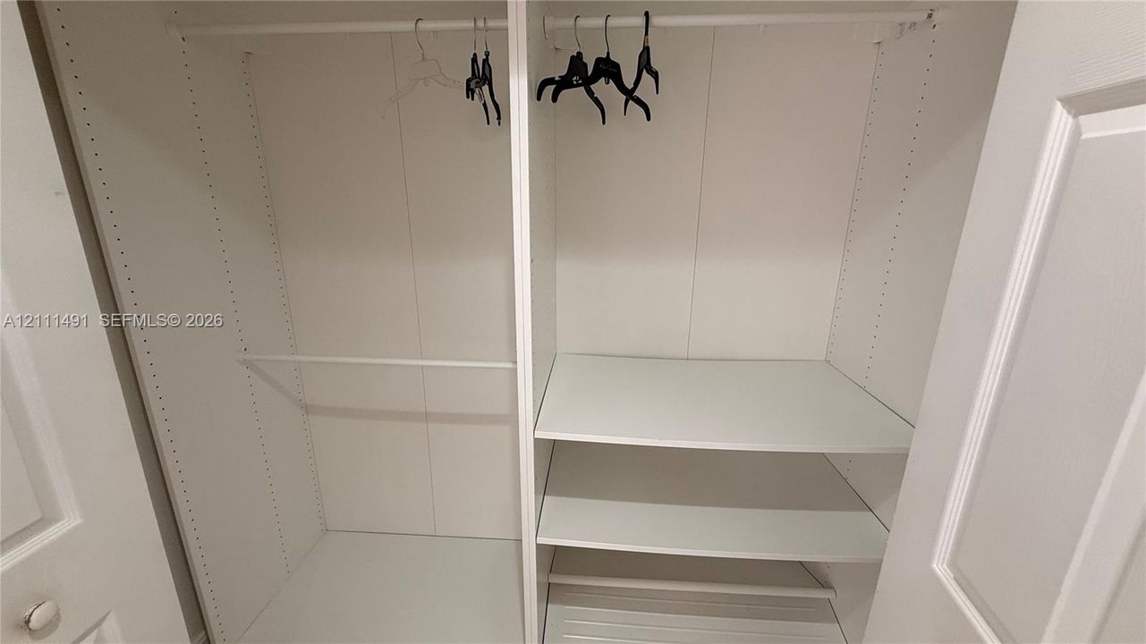 Built-in closet featuring white interior shelving, dual hanging rods, and adjustable shelving tracks