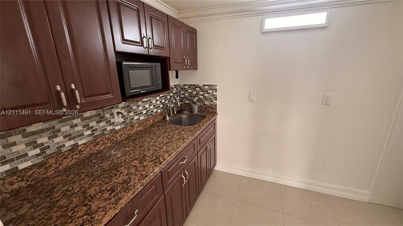 Dark wood-finish cabinetry, stone-texture countertop, mosaic tile backsplash, integrated stainless steel sink, and built-in microwave
