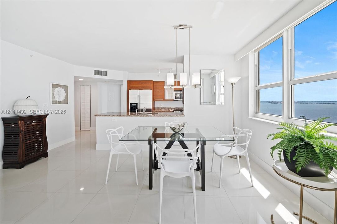 Open-concept kitchen and dining area featuring glossy tile flooring, wood-finish cabinetry, stone countertops, and floor-to-ceiling windows with water scenery