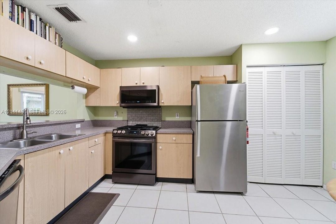 Kitchen featuring light wood-finish cabinetry, stone-style countertops, stainless steel appliances, a mosaic tile backsplash, and ceramic tile flooring