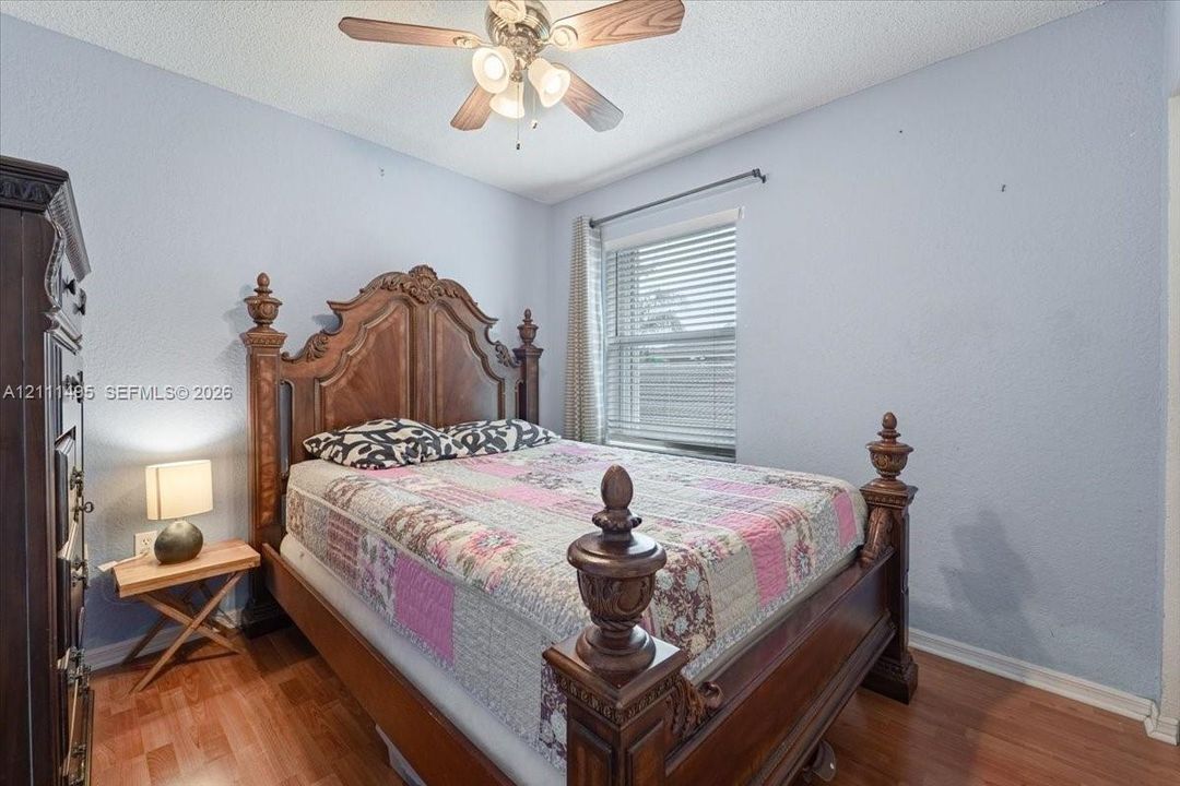 Bedroom featuring wood-finish flooring, a ceiling fan with integrated lighting, and a horizontal window fitted with blinds