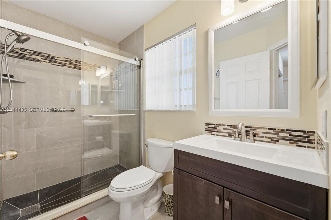 Bathroom featuring a dark wood-finish vanity with a rectangular integrated sink, glass-enclosed shower with large-format wall tiles and a decorative tile accent band, and a matching tiled shower floor
